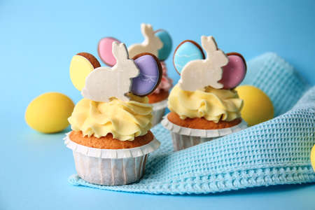 Tasty Easter cupcakes and eggs on blue background, closeup