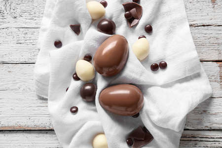 Chocolate Easter eggs with candies on white wooden background
