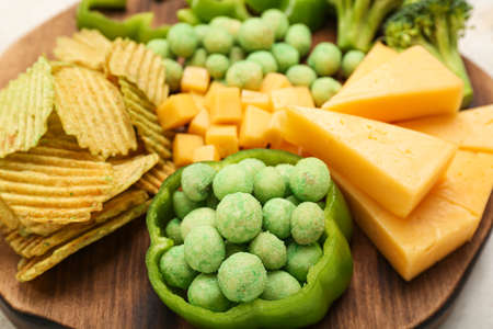 Wooden board with different snacks for St. Patrick's Day celebration on table, closeup