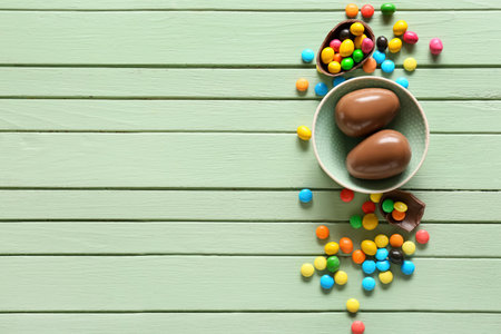 Bowl with chocolate Easter eggs and candies on green wooden backgroundの写真素材