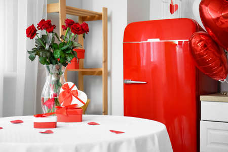 Gift boxes and vase with roses for Valentine's Day celebration on dining table in light kitchenの写真素材