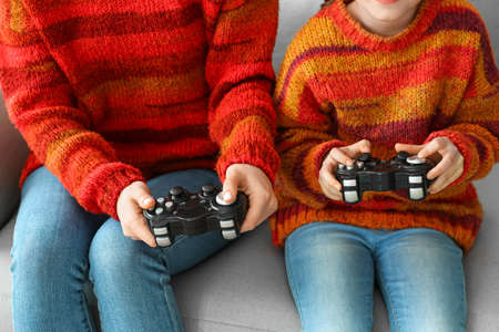 Little girl and her mother in warm sweaters playing video game at home, closeupの写真素材