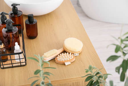 Body massage brushes and bottles with different cosmetic products on wooden tableの写真素材