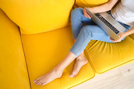 Barefoot woman with laptop on sofa at home