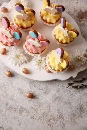 Board with tasty Easter cupcakes, eggs and flowers on light backgroundの写真素材