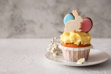 Plate with tasty Easter cupcake and flowers on light background, closeup