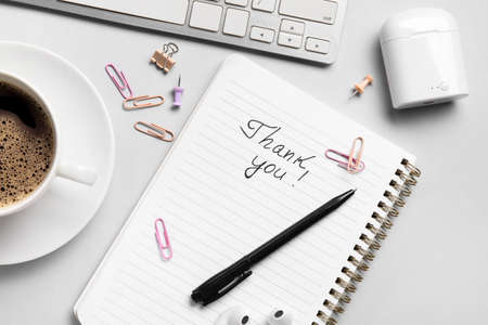 Notebook with text THANK YOU, cup of coffee, earphones and computer keyboard on gray backgroundの写真素材