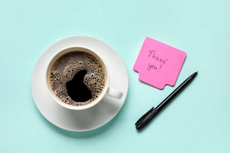 Sticky note with text THANK YOU, pen and cup of coffee on blue background