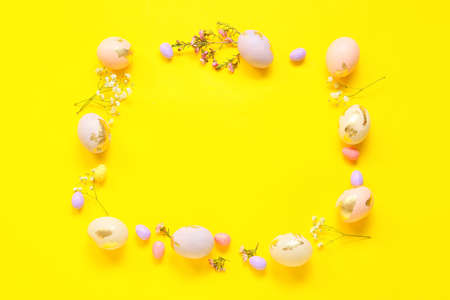 Frame made of Easter eggs and flowers on yellow background