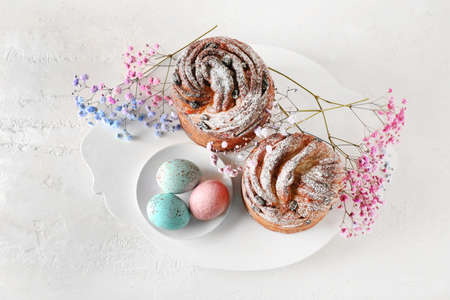 Wooden board with delicious Easter cake, eggs and gypsophila flowers on light background