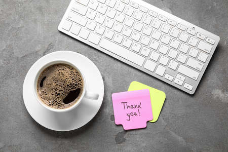 Sticky notes with text THANK YOU, computer keyboard and cup of coffee on dark backgroundの写真素材
