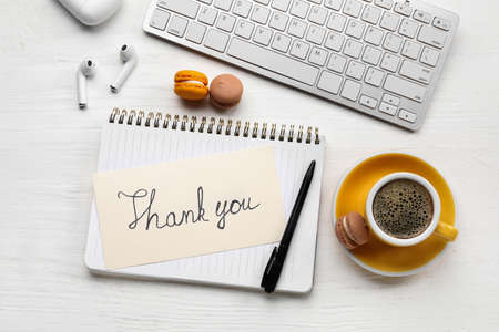 Notebook with text THANK YOU, macaroons, earphones, computer keyboard and cup of coffee on white wooden backgroundの写真素材