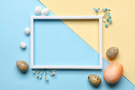 Easter composition with blank photo frame, eggs and flowers on color backgroundの写真素材