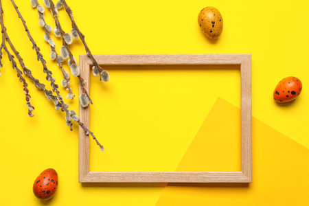 Easter composition with blank photo frame, eggs and willow branches on yellow backgroundの写真素材