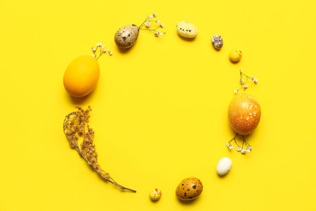 Frame made of beautiful Easter eggs and flowers on yellow background