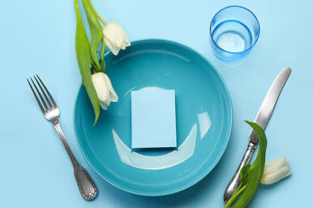 Table setting with blank card and tulips on color background