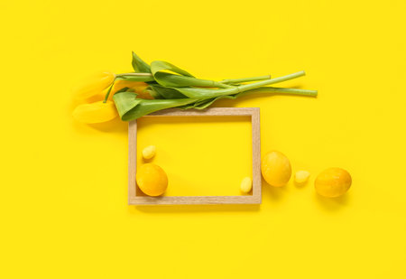 Beautiful composition with frame, Easter eggs and flowers on yellow backgroundの写真素材