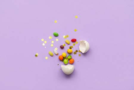 Composition with broken Easter egg and candies on purple background