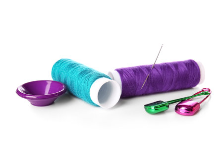Thread spools with needle, button and safety pins on white backgroundの写真素材
