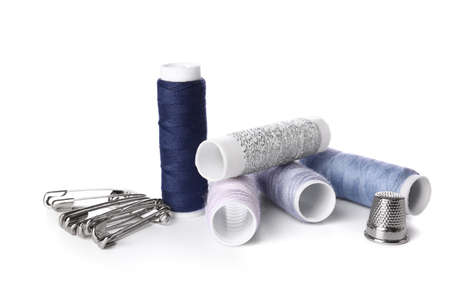 Different thread spools, safety pins and thimble on white background