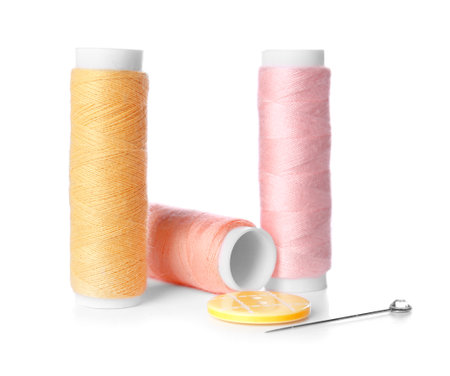 Thread spools, ball pin and button on white background