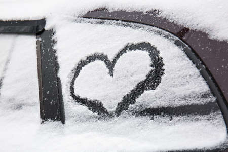 Heart symbol drawn on snow-covered carの写真素材