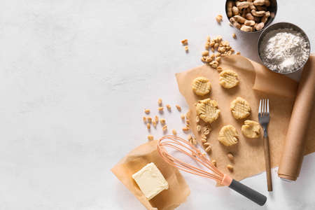 Parchment paper with uncooked peanut cookies and ingredients on white background