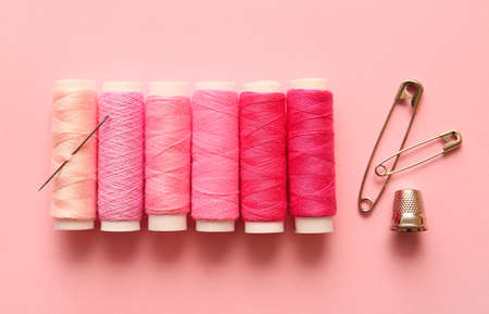 Multicolored thread spools, safety pins and thimble on color background
