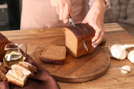 Woman preparing croutons with rye bread at kitchen table, closeup