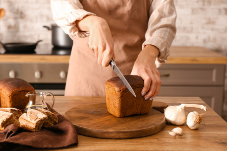 Woman preparing croutons with rye bread at kitchen table, closeup