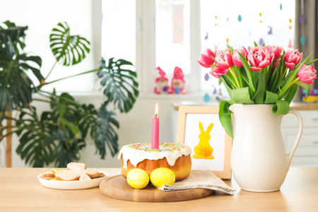 Easter cake, candle, eggs, cookies, picture and vase with tulips on counter in kitchen
