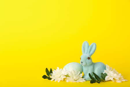 Beautiful Easter bunny, painted egg and flowers on yellow background