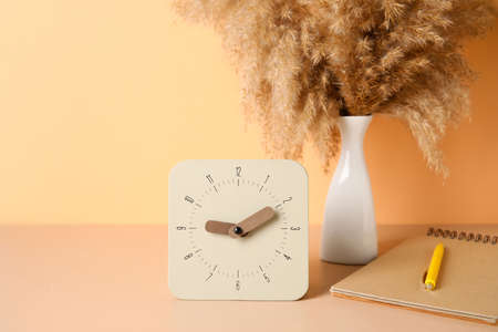 Alarm clock, notebook and vase with pampas grass on table near color wall