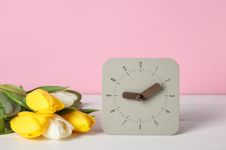 Alarm clock and bouquet of tulips on table near color wall
