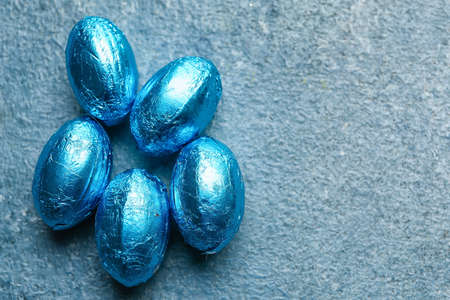 Easter eggs wrapped in blue foil on color background