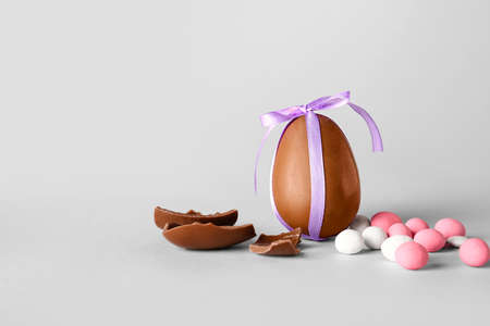Chocolate Easter egg with different candies on light background