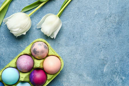 Holder with painted Easter eggs and tulips on color background