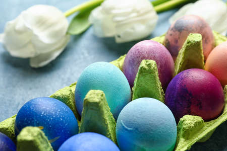 Holder with painted Easter eggs and tulips on color background
