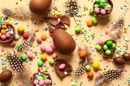 Composition with chocolate Easter eggs, different candies and feathers on beige backgroundの写真素材