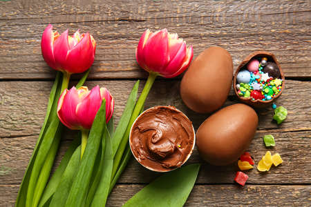 Composition with chocolate Easter eggs, different candies and flowers on wooden backgroundの写真素材