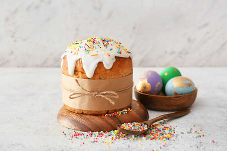Wooden board with delicious Easter cake and eggs on light background