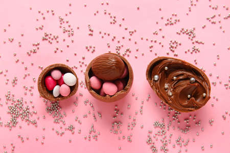 Composition with broken chocolate Easter eggs, different candies and sprinkles on pink background
