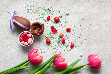 Composition with chocolate Easter eggs, different candies and flowers on light background