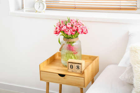 Bouquet of tulips and wooden cube calendar with date MARCH 8 on bedside table near light wall. International Women's Day celebrationの写真素材