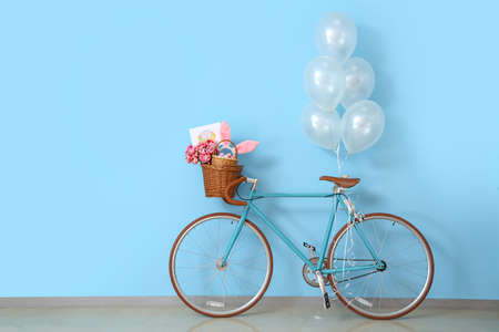 Bicycle with baskets, tulips, Easter eggs, greeting card and balloons near blue wallの写真素材