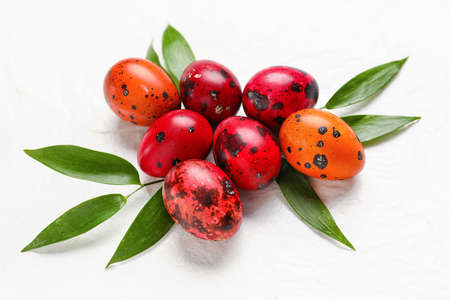 Composition with painted Easter eggs and green leaves on light background