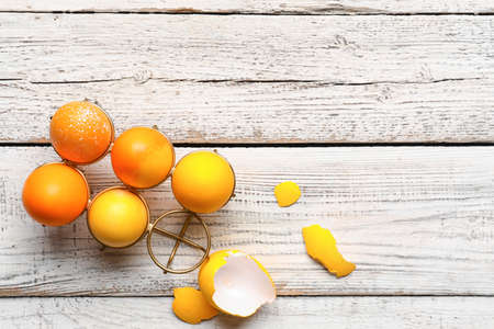 Holder with painted Easter eggs and eggshell on white wooden backgroundの写真素材