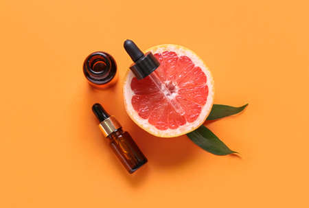 Bottles with essential oil and half of grapefruit on color backgroundの写真素材