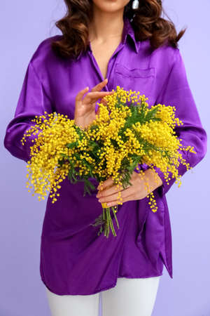 Beautiful young woman with bouquet of mimosa flowers on lilac backgroundの写真素材