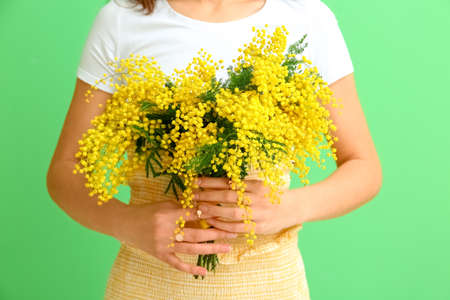 Beautiful young woman with bouquet of mimosa flowers on green backgroundの写真素材
